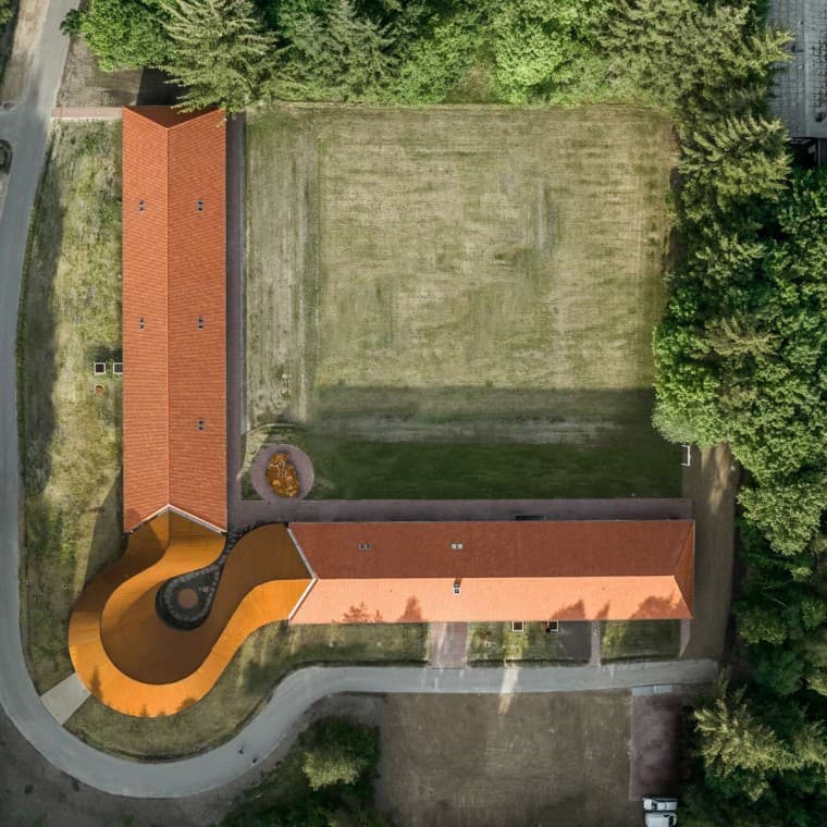 Pogled odozgo pokazuje okruglu novu zgradu koja povezuje dve istorijske zgrade sa popločanim krovovima. (© R_Hjortshoj) Pogled odozgo pokazuje okruglu novu zgradu koja povezuje dve istorijske zgrade sa popločanim krovovima. (© R_Hjortshoj)